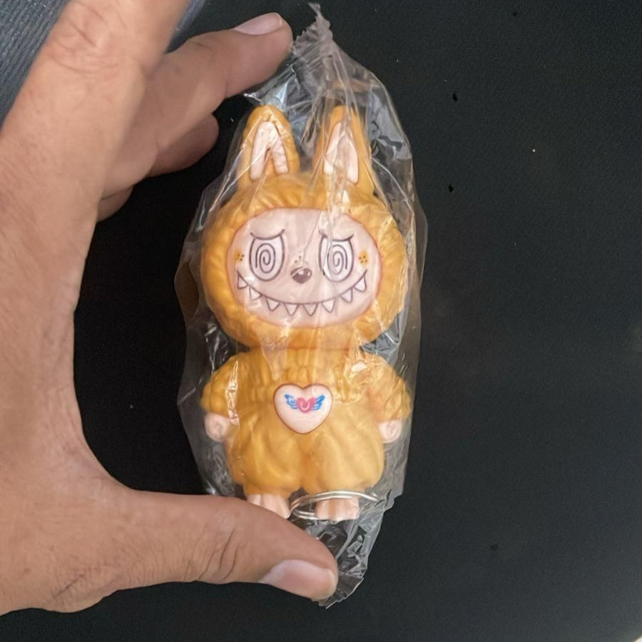Hand holding a small orange character toy wrapped in plastic on a black surface.
