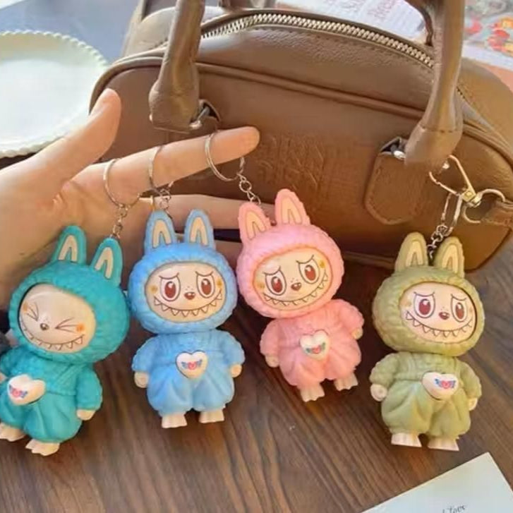 Four colorful keychains shaped like cartoon characters in bunny costumes on a wooden surface.